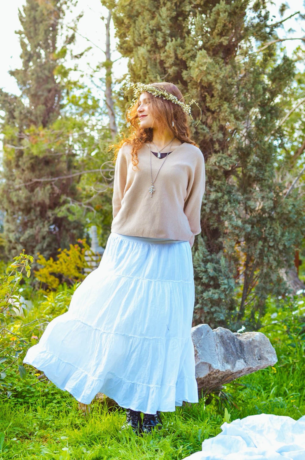 Woman in a flowing pale-blue tiered skirt and knit top in a sunny garden