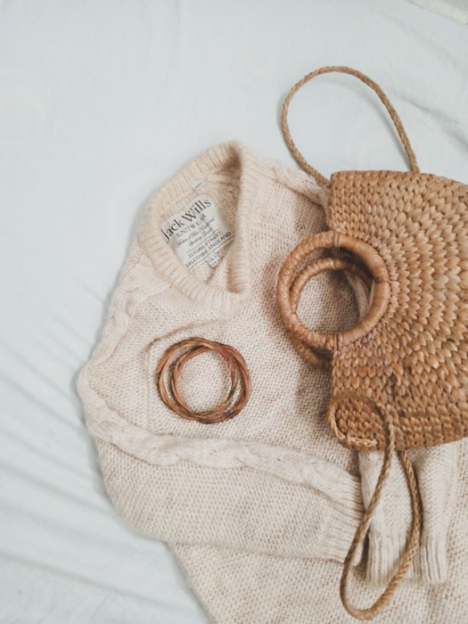 Cream knit sweater with a round woven bag and wooden bangles