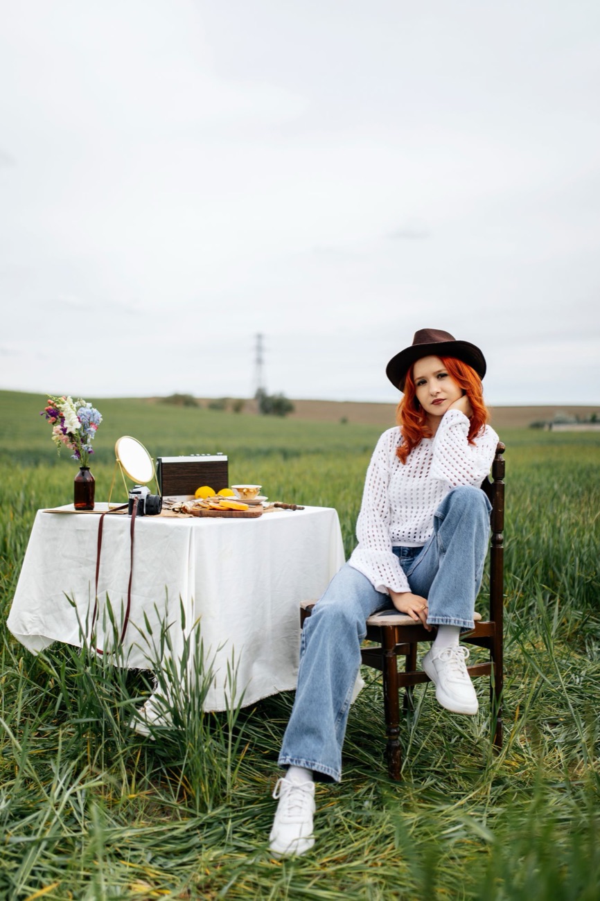 Woman in a hat and white blouse sitting at a picnic table in an open field