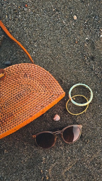 Woven orange bag with sunglasses and bangles on sand