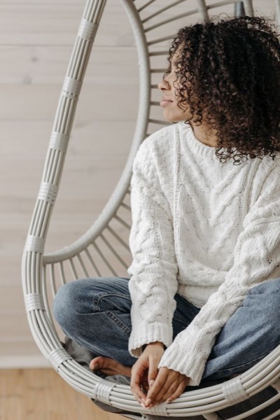 Woman in a white cable knit sweater sitting in a hanging chair